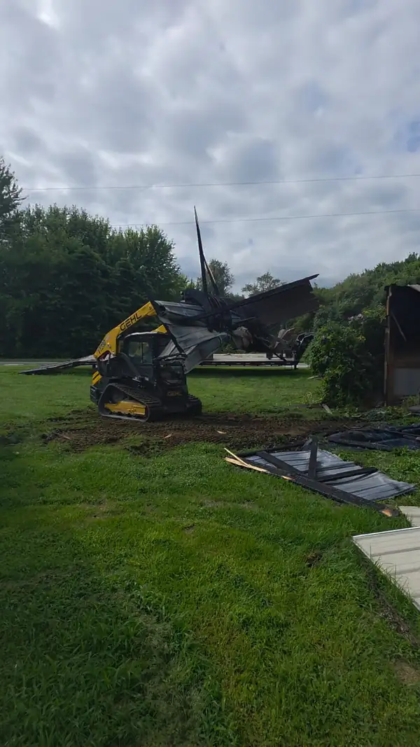 Compact track loader with a grapple lifting metal roofing during a small structure demolition