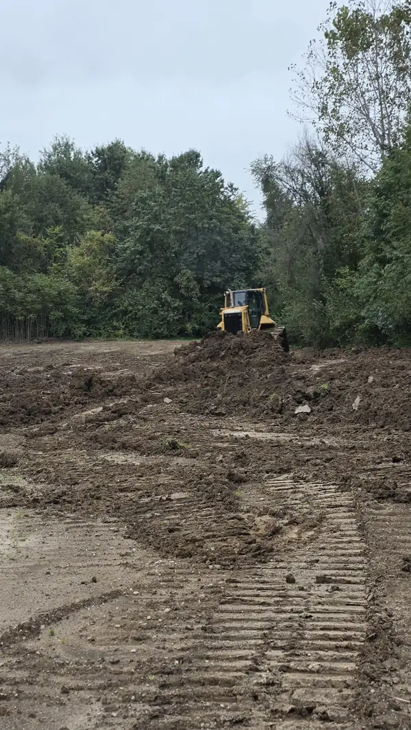 Bulldozer working a mound of soil with track marks in the foreground