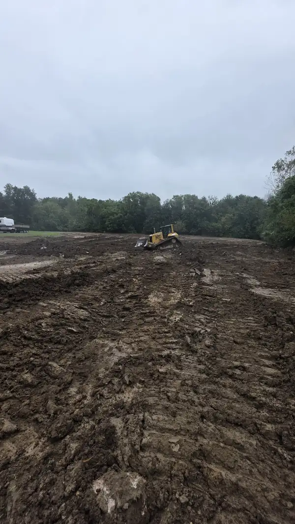 Bulldozer rough grading a wide muddy site under overcast skies