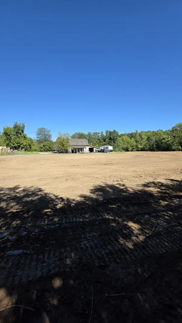 Wide leveled dirt field with a house and outbuilding in the distance