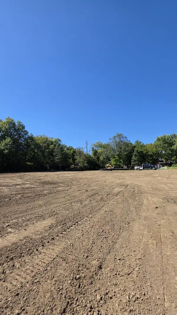 Large smooth-graded dirt area with trucks and equipment at the far tree line