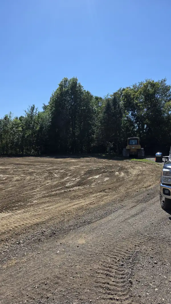 Graded dirt area tying into a gravel drive with a dozer parked near the trees