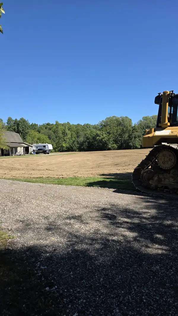Freshly graded field seen from a gravel drive with a bulldozer at the edge of the frame