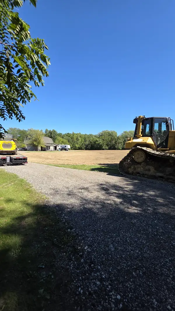 Bulldozer parked on a gravel drive beside a freshly graded field