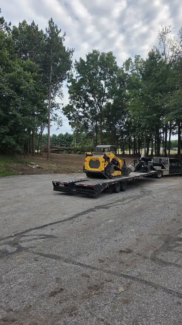Compact track loader loaded on a flatbed trailer beside a cleared lot