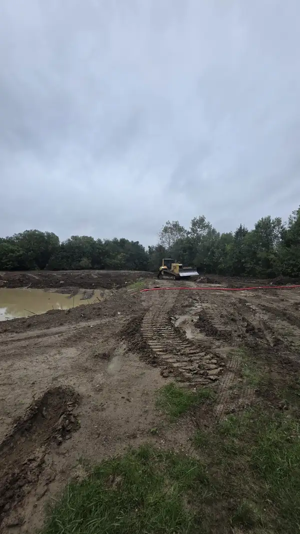 Bulldozer shaping the bank beside a water-filled pond excavation